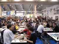 Dozens of people playing games at tables in front of a Rio Grande Games sign