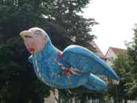 Sculpture of a sparrow with a human face and a body decorated to show two people jousting over water