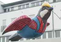 Sculpture of a sparrow wearing a plaid shirt, bib overalls, and a construction helmet