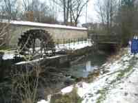 Waterwheel in stream, with snow-covered banks