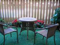 Wicker chairs and table on a patio with brown picket fence and fake plants