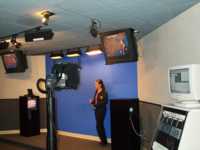 Tour guide standing in front of a blue screen while monitors show her in front of a weather map